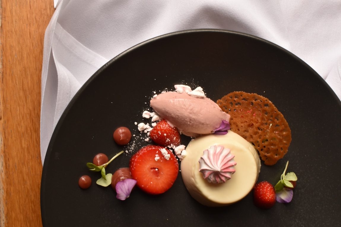 An elegantly plated dessert at The Square Club, a renowned party venue in Bristol. The black plate features a panna cotta-like dessert garnished with fresh strawberries, edible flowers, and a light scoop of sorbet. The high-quality presentation highlights the exquisite catering options available for parties and events at this Bristol venue, making it ideal for those looking to host upscale celebrations.