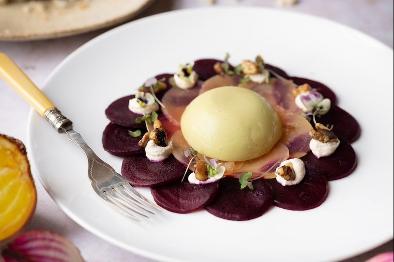 An artfully presented dish at The Square Club, one of the finest party venues in Bristol. The white plate features a stunning arrangement of thinly sliced beetroot, creamy cheese, and garnishes of microgreens and walnuts. This elegant dish highlights the venue’s excellent catering services, making The Square Club a top destination for upscale dining and celebrations in Bristol.