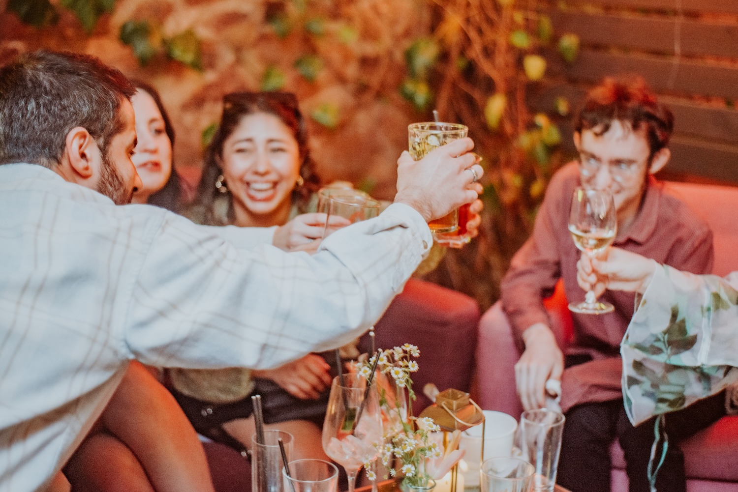 A group of people toasting with drinks in hand at The Square Club, a popular party venue in Bristol. A man in a checkered shirt raises a glass toward the group, while others, including women, smile and laugh in the background. The dim, cozy lighting and relaxed setting suggest an intimate gathering, ideal for private parties or celebratory events at this iconic venue.