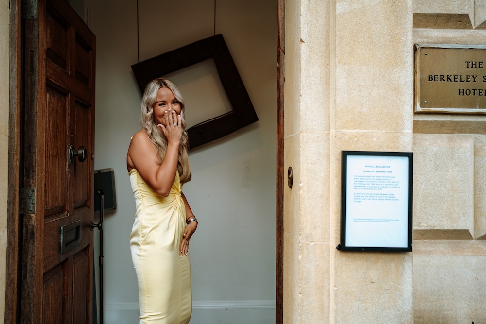 In this image, a guest in a pastel yellow dress covers her mouth in a joyful, candid moment outside The Square Club, a popular wedding venue in Bristol. The stone facade and large wooden door of the venue provide an elegant yet understated backdrop for this playful scene. With its charming and historic architecture, The Square Club is the perfect wedding venue in Bristol for capturing both formal and informal moments, allowing guests and bridal parties to relax and enjoy the day.