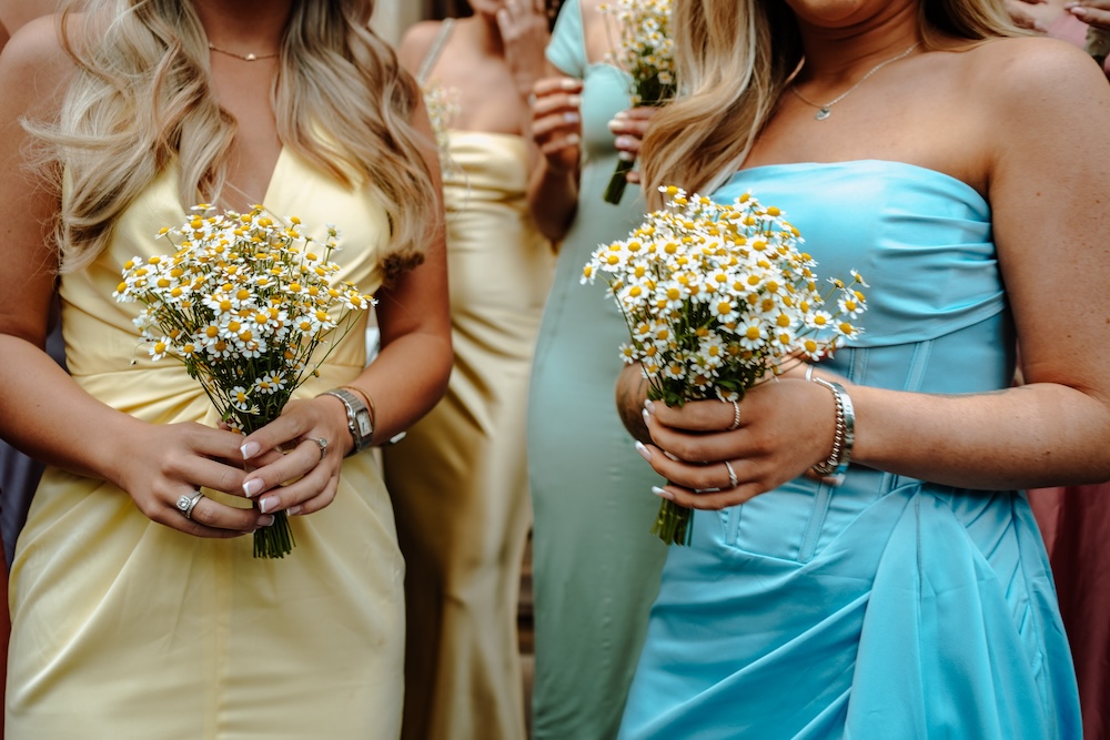 This close-up image captures the bridesmaids at The Square Club, a sophisticated wedding venue in Bristol, holding small daisy bouquets. Their pastel-colored dresses in yellow and blue add a soft, summery touch to the ceremony. The delicate flowers and vibrant dresses reflect the joyful yet elegant atmosphere of the wedding, while The Square Club provides a picturesque backdrop with its charming location in the heart of Bristol. This venue is ideal for couples seeking both style and warmth for their wedding celebration.