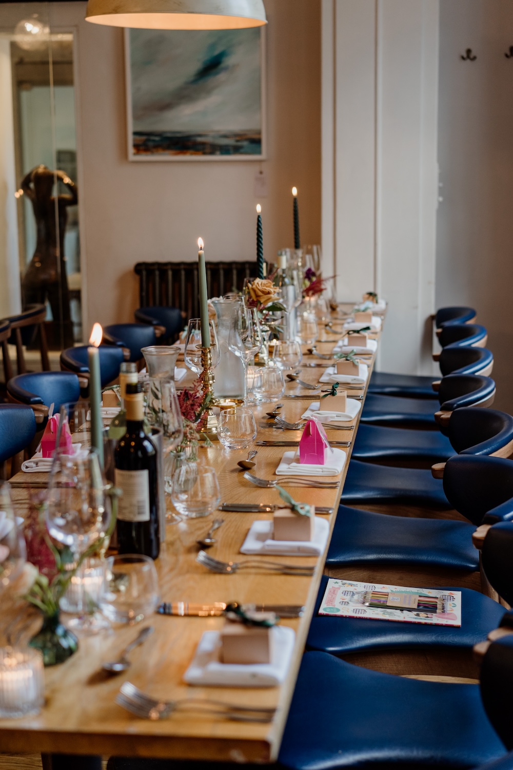 A closer view of the beautifully set dining table at The Square Club, a wedding venue in Bristol. The long table is adorned with candles, wine bottles, and neatly folded napkins, exuding elegance and attention to detail. The modern lighting fixtures above add a warm glow to the room, creating a cozy and inviting space for wedding guests to enjoy. The Square Club is known for offering an intimate and stylish venue for weddings in the heart of Bristol.